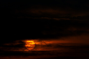 A rising sun shows through dark clouds.