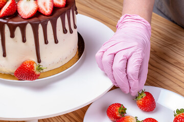 The girl decorates the cake with fresh red strawberries. A plate of cake on the table and a saucer...