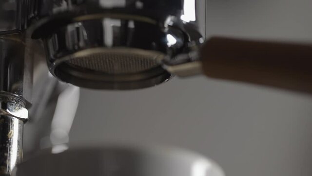 Slow motion low angle shot of espresso extraction from naked portafilter into white cup