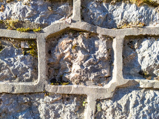 Old stone wall - irregular blocks bound with cement mortar making decorative raised margins. Close-up of rough surface on grey rock.