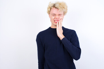 Young handsome Caucasian blond man standing against white background touching mouth with hand with painful expression because of toothache or dental illness on teeth.