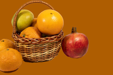 Isolate on a brown background. The basket contains green apples, oranges and tangerines. There are pomegranates and tangerines nearby.