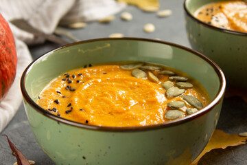 Bowl with pumpkin cream soup and seeds on a cement surface with autumn leaves