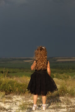 a little girl in a black field stands with her back