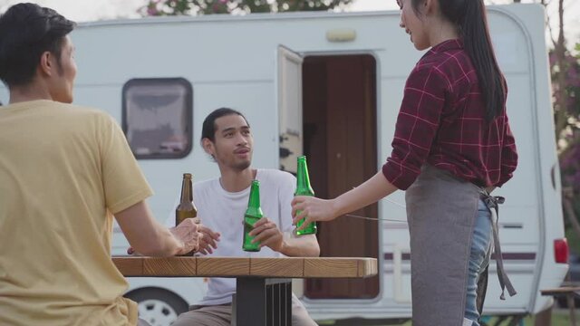 Asian friends toasting and drinking bottles of beer at outdoor party.