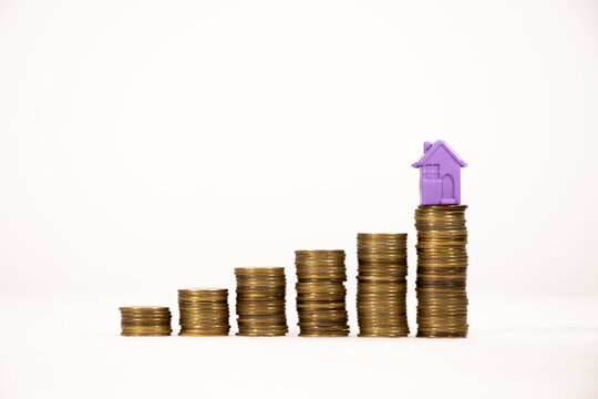 .Saving money for real estate / financial investment / mortgage. Small house with growing coins as a concept of saving money to buy a new residential asset.