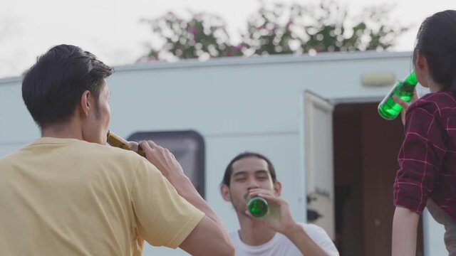 Asian friends toasting and drinking bottles of beer at outdoor party.