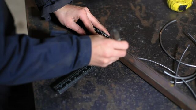 Selective focus of hands of young female blacksmith, making measuring points on iron square pipe with ruler and marker pen on work table in workshop
