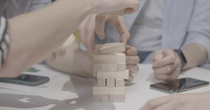 Male and female hands building Jenga tower on table. Unrecognizable adult Caucasian men and women playing game indoors. Friends having fun. Leisure and friendship concept. Cinema 4k ProRes HQ.