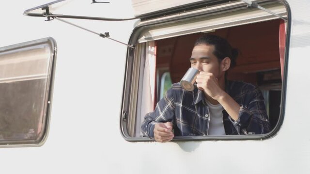 Smiling male sitting inside caravan drinking coffee in summer morning.