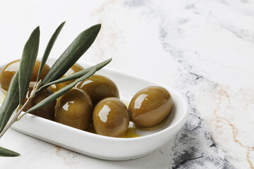 Composition of green olives in oil, olive branch, on a marble background. Space for text.