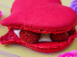 Macaroon with raspberries and cream.
Heart shaped pink macaroons with raspberries and cream on a yellow background, close-up side view.