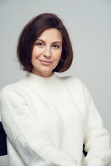 posing serious confident young woman brunette of European appearance, looking at the camera smiling. White warm stylish jacket