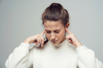 covers her ears with her hands loud music playing, a young confident woman of European appearance. Clothing white fluffy warm stylish jacket. copy space