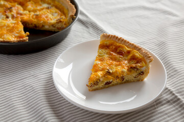 Homemade Bacon Quiche with Eggs and Cheddar Cheese on a white plate, side view. Close-up.