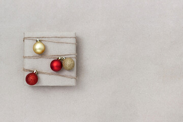 Handmade gift box is decorated with natural rope and four Christmas balls on kraft paper background. Copy space.
