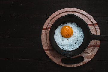 fried egg with salt, pepper, oil, cooked to the point in an iron pan, on a kitchen table, on a rustic black background