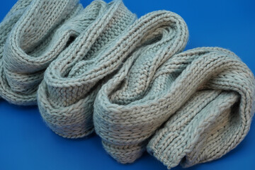 Long warm gray winter knitted scarf, close-up on a blue background.