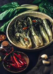 Swiss chard (Bietola) recipe with hot peppers, garlic, wine vinegar, herbs and olive oil on the dark rustic background. Seasonal vegetarian cuisine. Vegan food cooking preparation