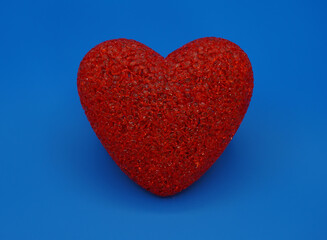 Bright red heart made of small plastic granules, close-up on a blue background.