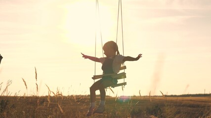 Fototapeta na wymiar Amusement park dream concept. Happy girl swinging on a swing in the park at sunset. child plays with wooden swing, childhood dream, airplane pilot flights to the sky. A happy family