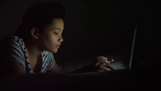 Portrait of young girl typing on a laptop in the dark
