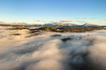 Fototapeta premium Aerial view of a small distant village houses on hill top in fall foggy mountains at sunrise.