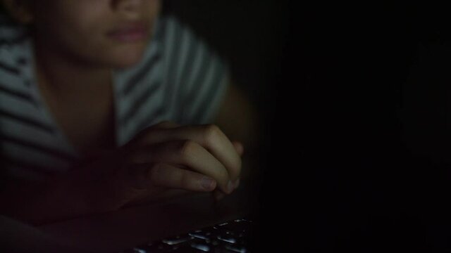 Young girl typing on a laptop in the dark at night