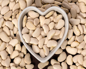 Large lima beans in a heart-shaped bowl background and texture. Top view.