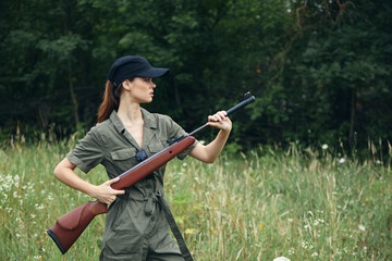 Woman soldier Holds a gun in a side view against the background of the forest 