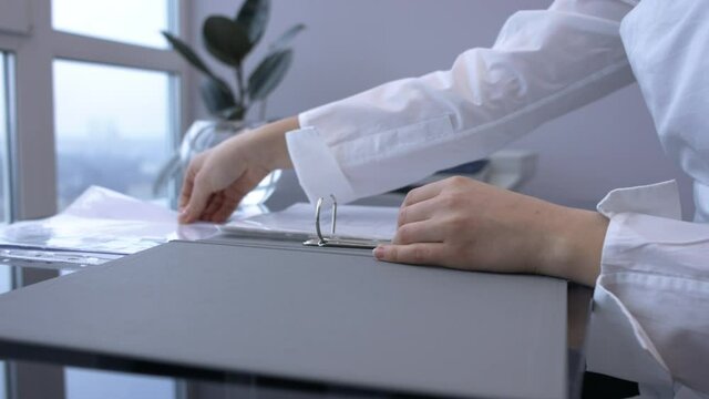 Female hands unlock binder ring, insert file in folder, closes folder