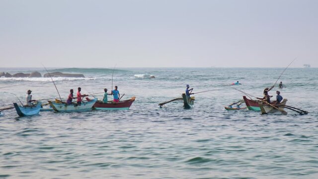 Local people catch fish on well-shaped rowing boats in calm ocean waves against tourists and surfers slow motion. Concept marine fishing and travel