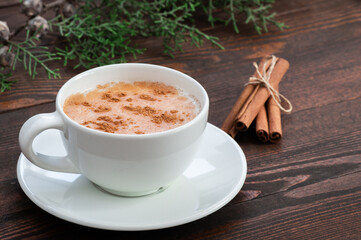 white cup of salep milky traditional hot drink of Turkey with cinnamon powder and sticks on rustic vintage wooden table. Sahlep background