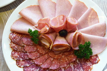 sliced cold snacks in the form of sausages and smoked meats are beautifully laid out on a festive dish