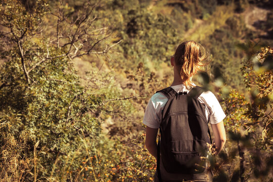 Young girl traveler with backpack stands with back in forest during solo weekend trip. Hiking and daily walks, trekking