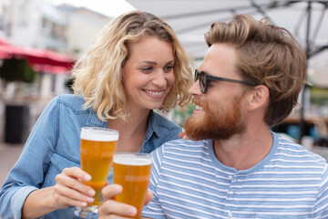 happy smiling couple toasting and drinking beer at outdoor pub