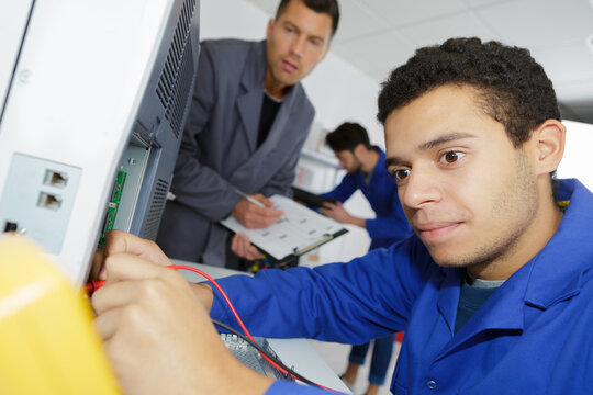 Young Apprentice Electrician Using Multimeter On Electrical Appliance