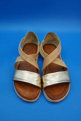 Women's summer beige and gold sandals made of genuine leather on a white rubber sole. Close-up, blue background.