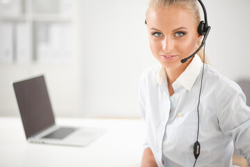 Portrait of smiling receptionist using laptop computer and headset at office desk