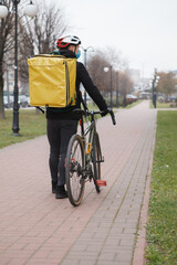 Obraz premium Rear view shot of a deliveryman wearing medical mask and thermo backpack, walking in the city after riding bicycle