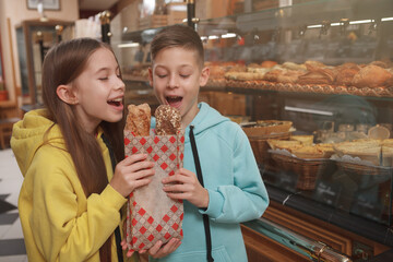 Cheerful young twins biting delicious freshly baked bread at bakery shop, copy space