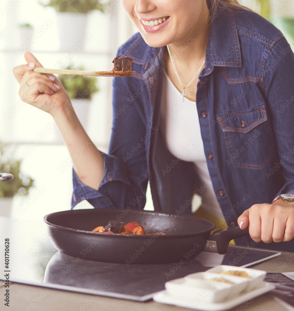 Wall mural Young woman cooking healthy food holding a pan with vegetables is it. Healthy lifestyle, cooking at home concept