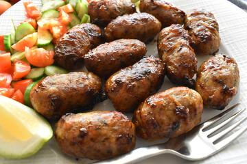 Sheftalia: Cypriot Lamb and Pork Sausages. Grilled Sausages with Fresh Vegetables (Cucumber and Tomato) on a White Plate. Traditional Cypriot food.	
