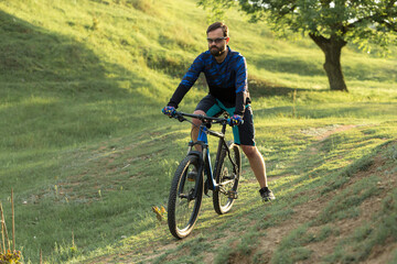 Fototapeta premium Cyclist in shorts and jersey on a modern carbon hardtail bike with an air suspension fork standing on a cliff against the background of fresh green spring forest