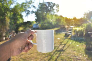 Hand of people holding to white coffee cup for drink. Beautiful and fresh time of people holding coffee cup for drink isolated on garden background with soft sunlight.