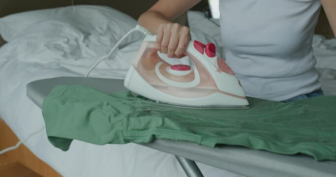 Woman iron clothes with iron on ironing board