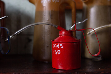 Close up of a red oil can in front of some oil jugs