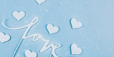 White hearts on blue.
White hearts and the word love paper cut on the left on a blue background with a place for text on the right, top view close-up.