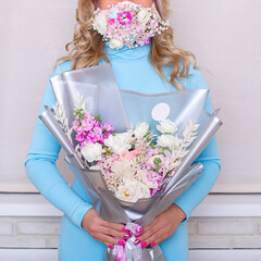 
Female hands of beautiful woman in blue dress and face mask holding bouquet of flowers