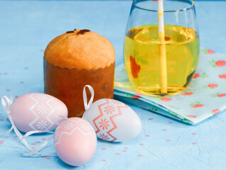 
Easter cake, orange juice in a glass and eggs on a blue background, close-up side view.